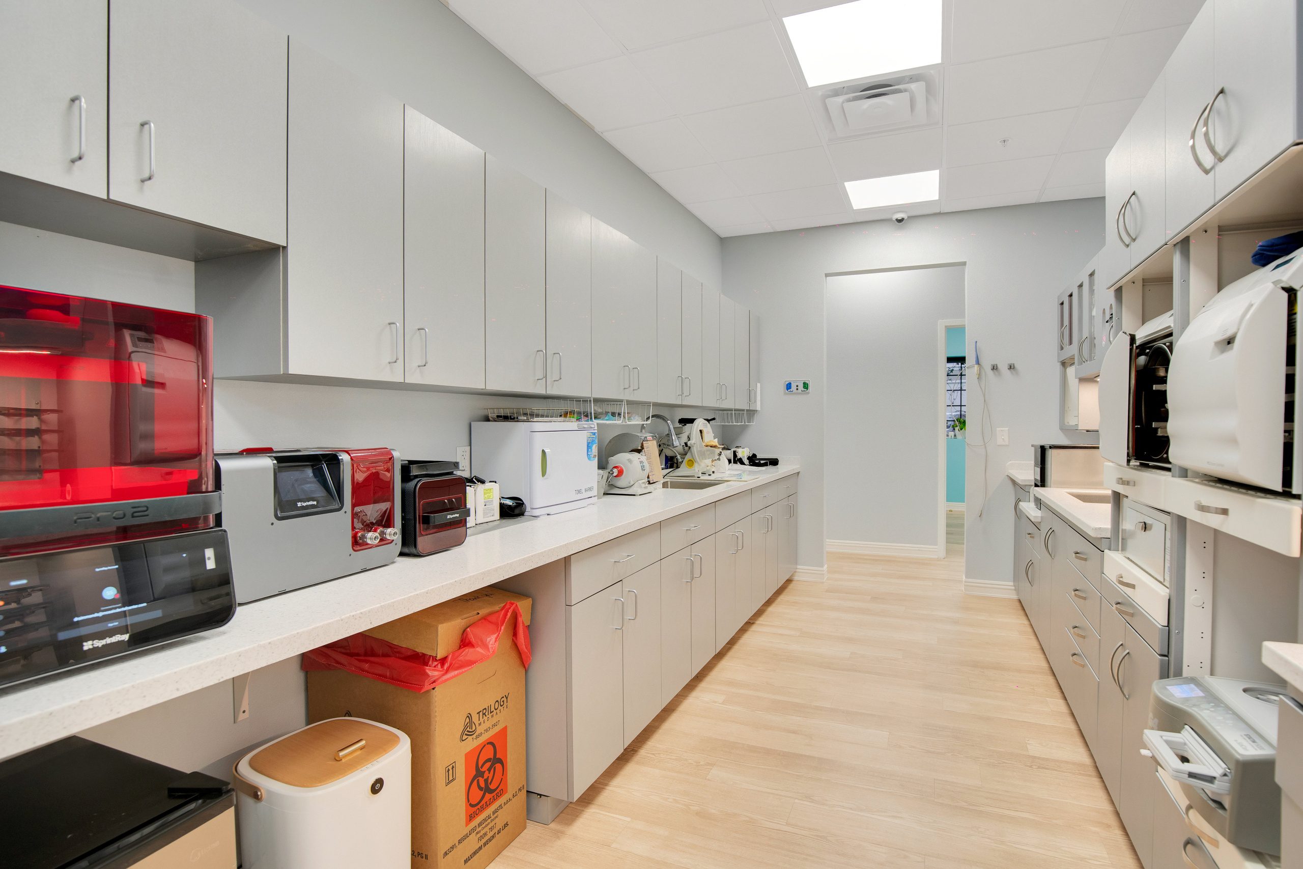 A modern lab or clinic break room with countertops, cabinets, and various appliances along the walls.
