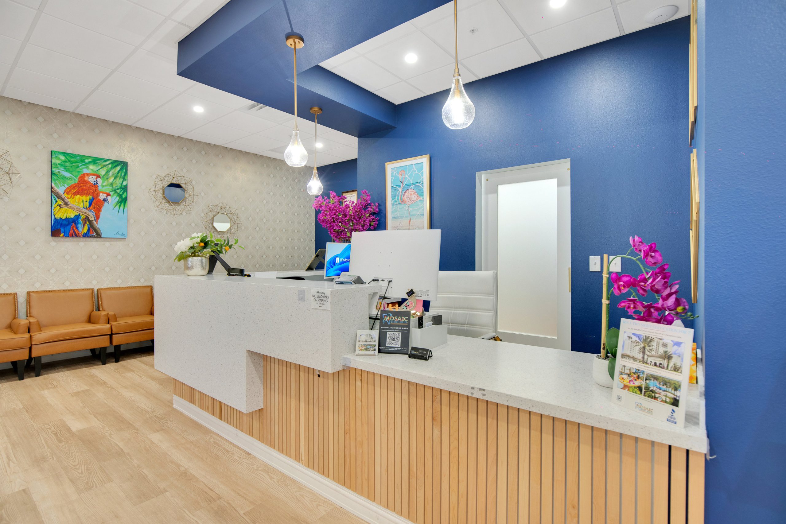 A bright, modern reception area with a white speckled counter, light wood paneling, blue accent wall, and warm tan seating.